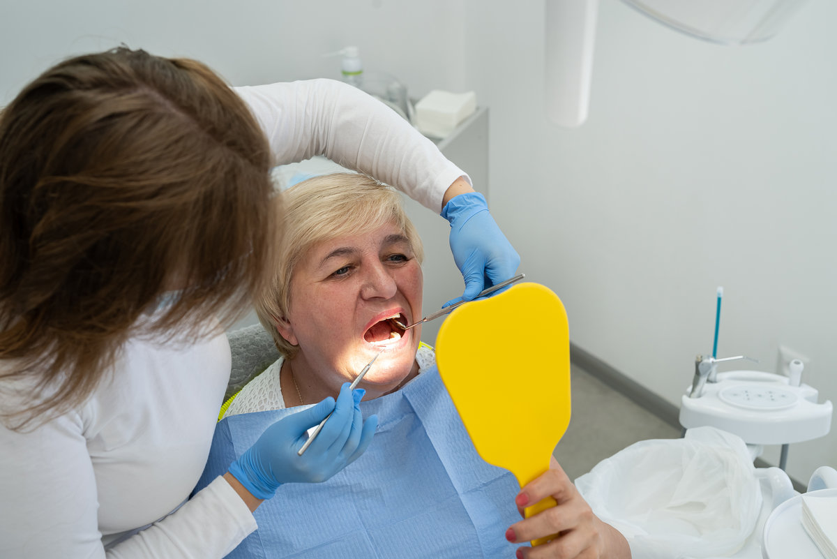 female dentist with elderly woman looking together to the mirror in the dental office. Healthy lifestyle